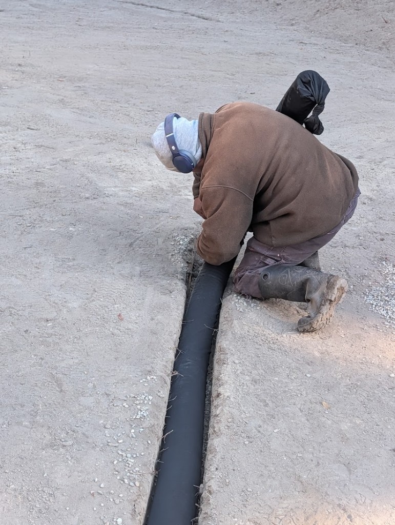 Crew member setting filter-socked drainage pipe in a trench