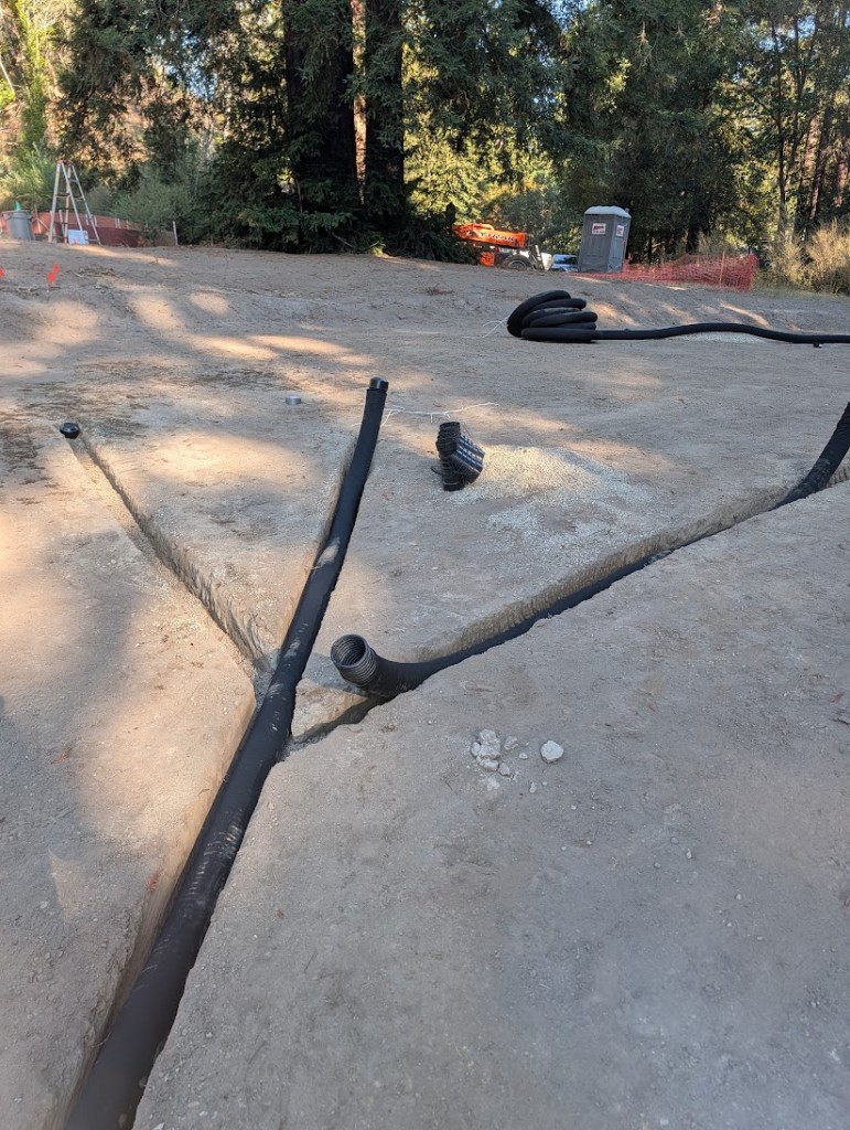 Perforated drainage pipe laid on pea gravel in trenches on a green