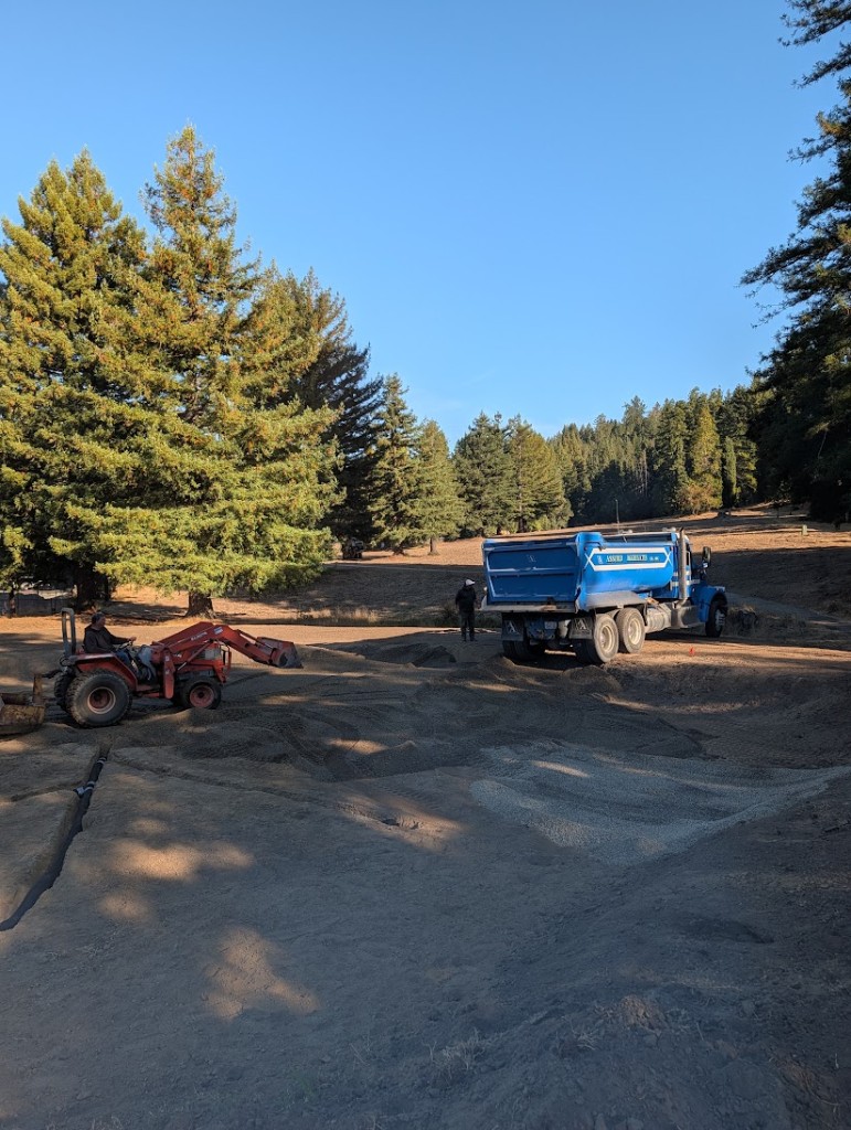 Dump truck and tractor placing gravel over drainage on the 12th green
